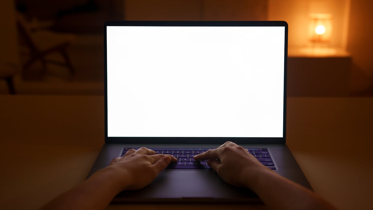 Person sitting by a window looking out thoughtfully with a laptop beside them